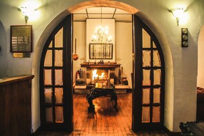 Un arco de entrada conduce a una habitación con chimenea, candelabro y mesa de madera.