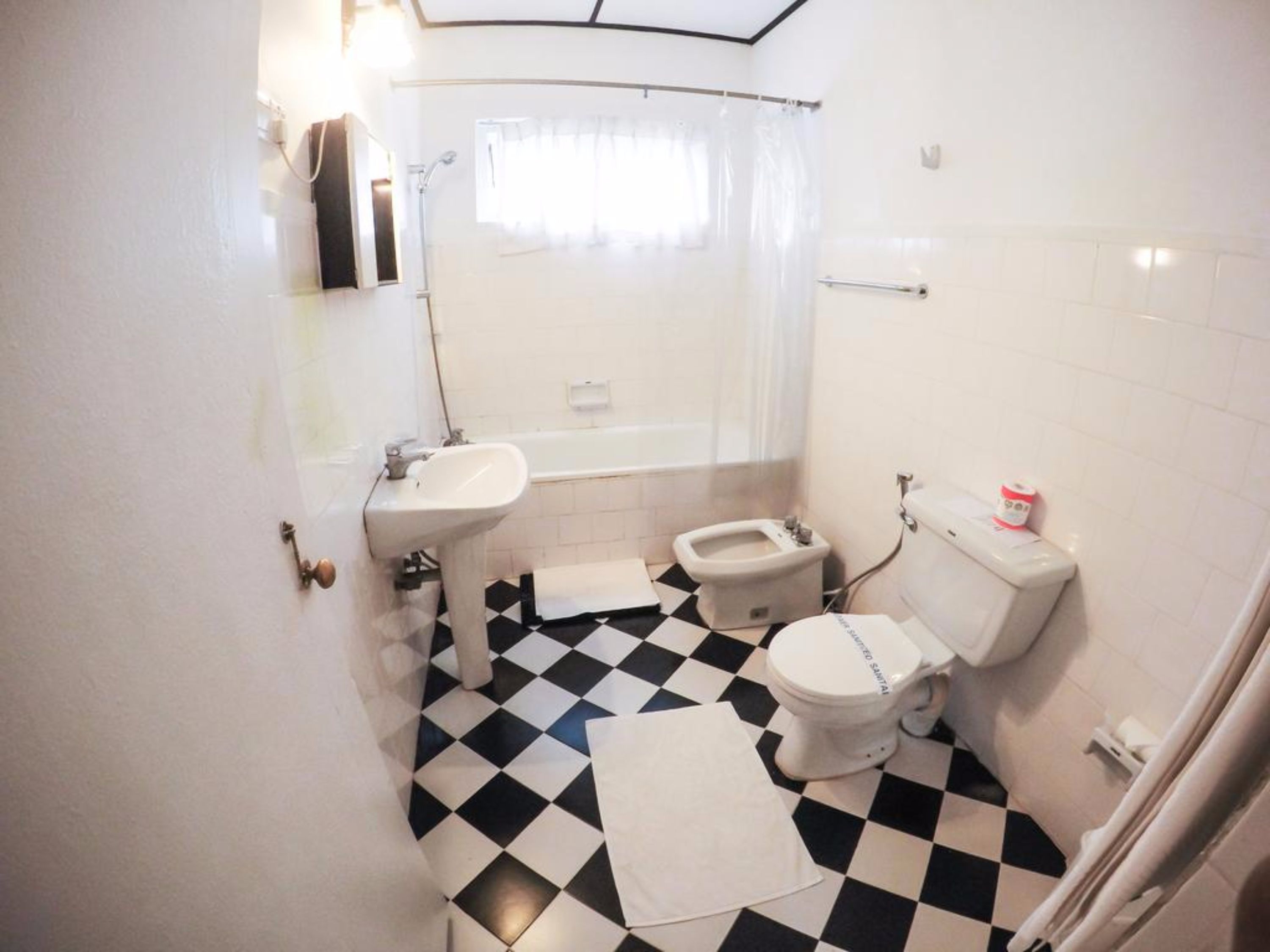 Ein Badezimmer mit Schachbrettboden, Waschbecken, Toilette und Duschbereich.