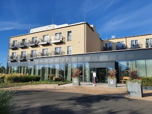 A modern hotel with a glass facade, multiple balconies, and a landscaped entrance.
