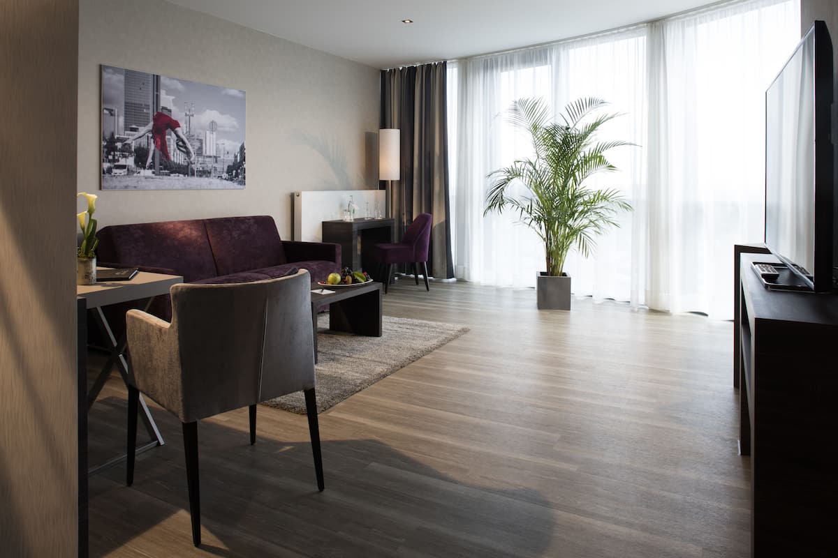 A modern living room with a sofa, chairs, a coffee table, a TV, and a large window with curtains.