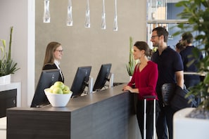 A reception desk with three computer monitors, a white bowl of apples, and a potted plant.