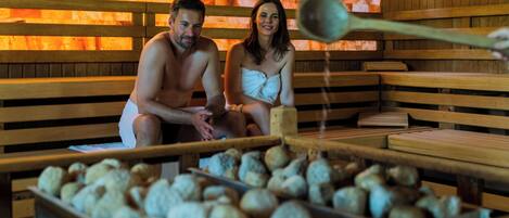A sauna with wooden benches and a stone wall in the background.