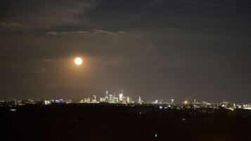 Un paisaje urbano nocturno con una luna llena destacada en el cielo y edificios iluminados a lo lejos.