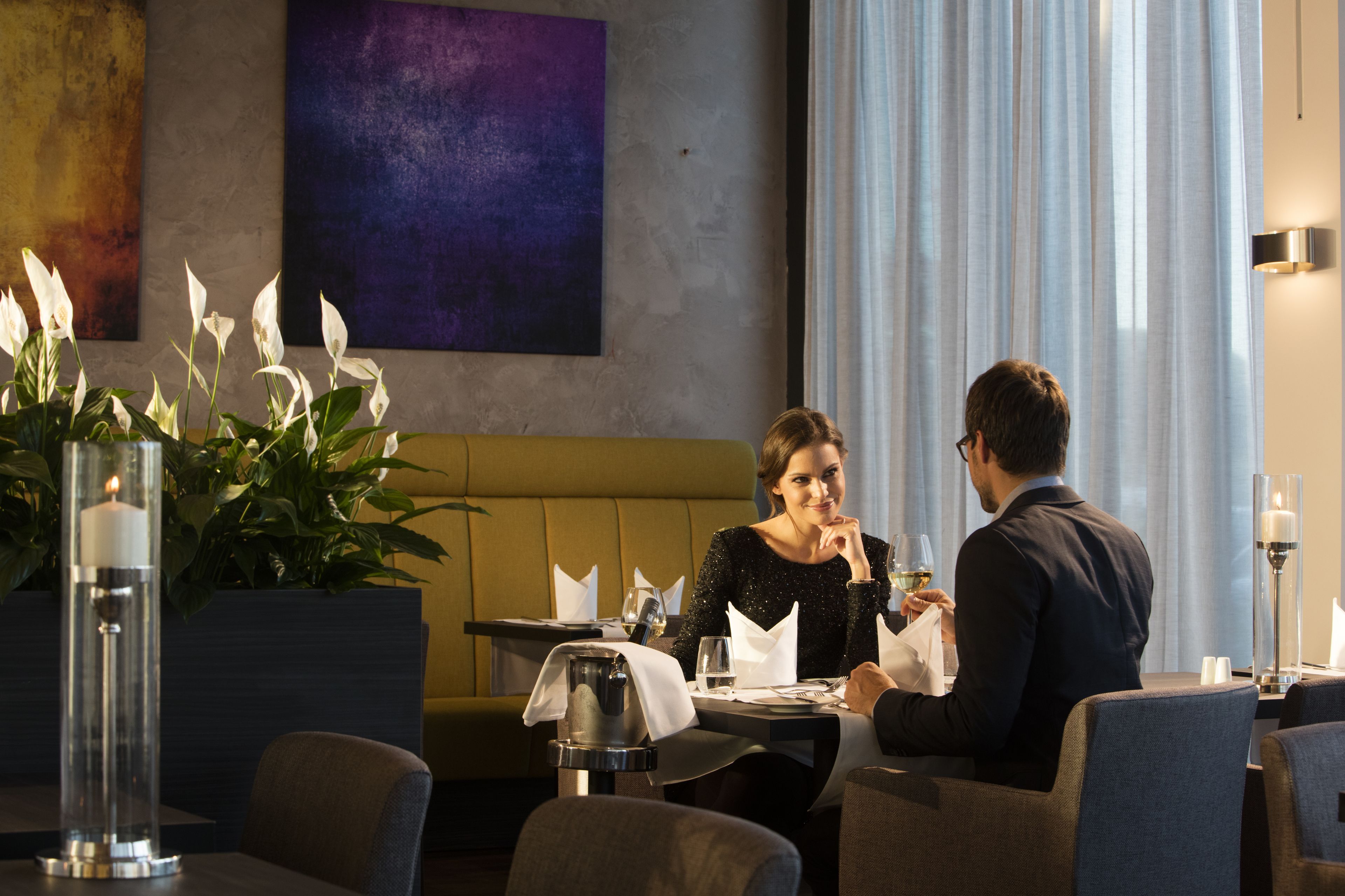 Een eethoek met een tafel gedekt voor twee personen, een bank en een potplant.