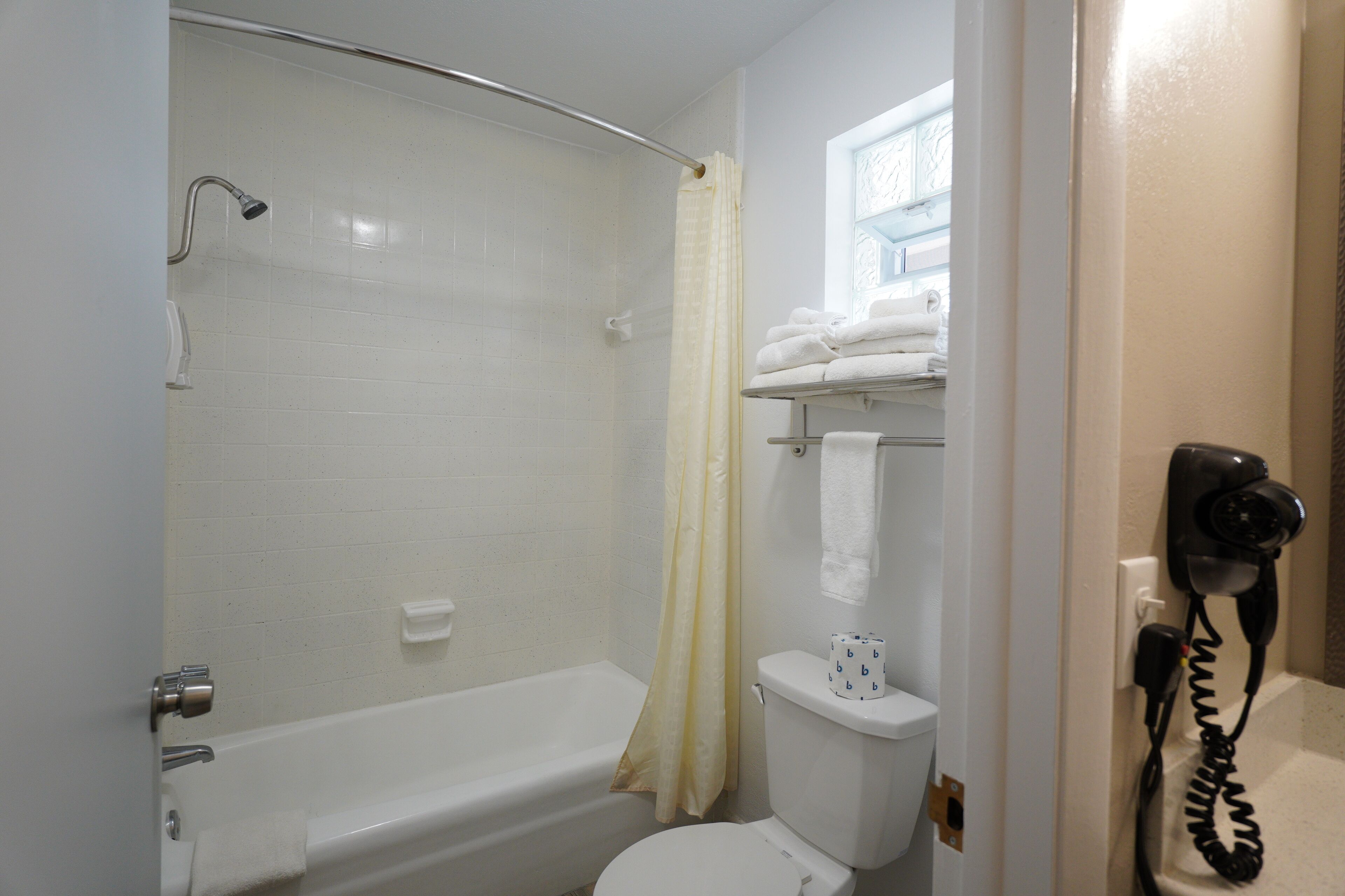 Un baño con bañera, inodoro y un secador de pelo en la pared.