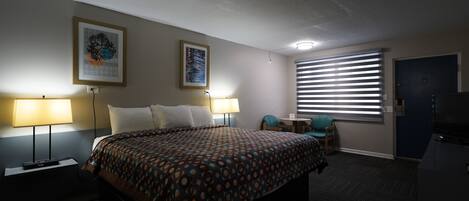 Une chambre d’hôtel comprenant un lit, deux lampes de chevet, un bureau avec une chaise, une télévision et une fenêtre avec des stores.