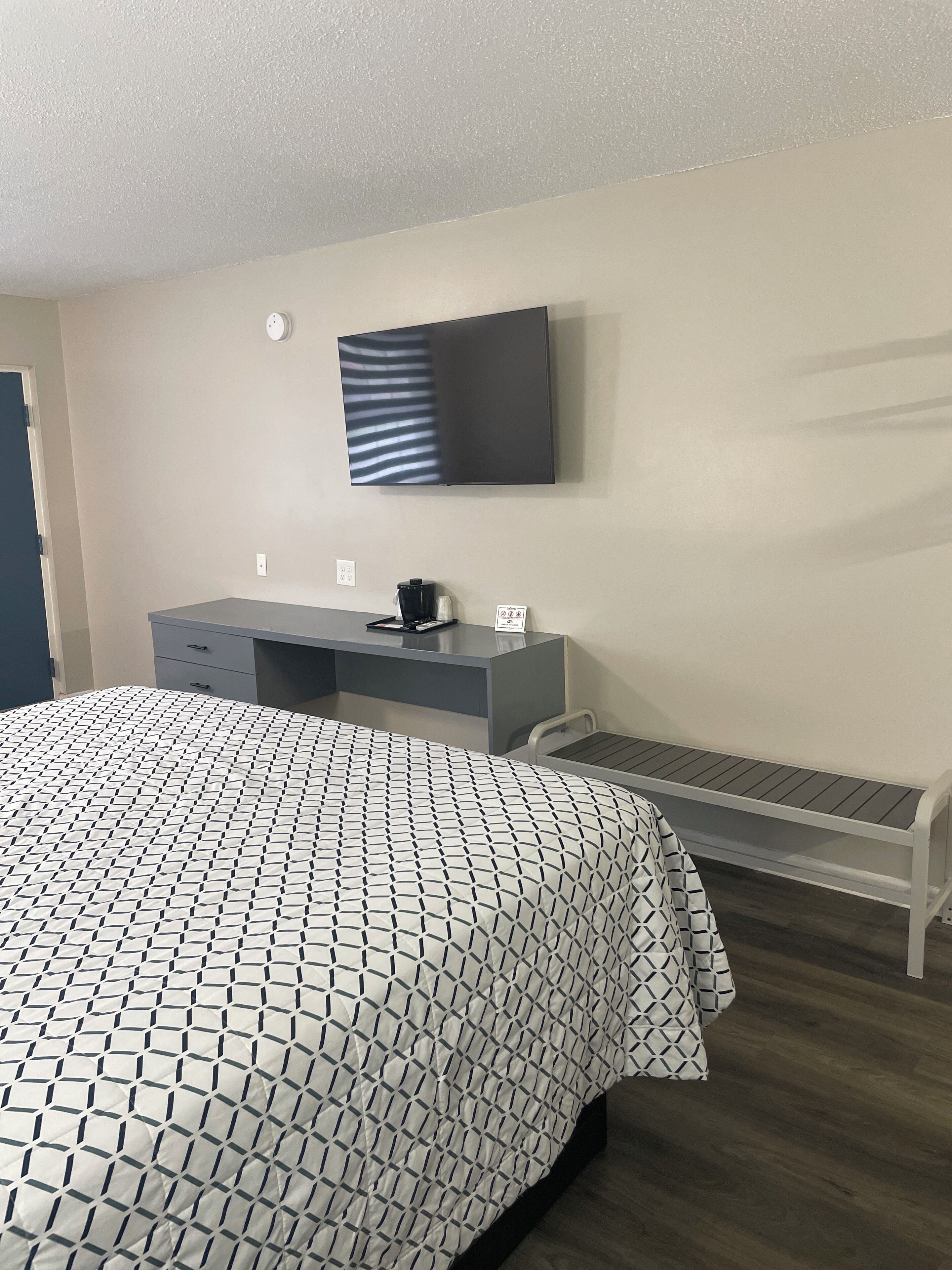 Een slaapkamer met een bed, bureau, stoel, televisie en koffieapparaat.