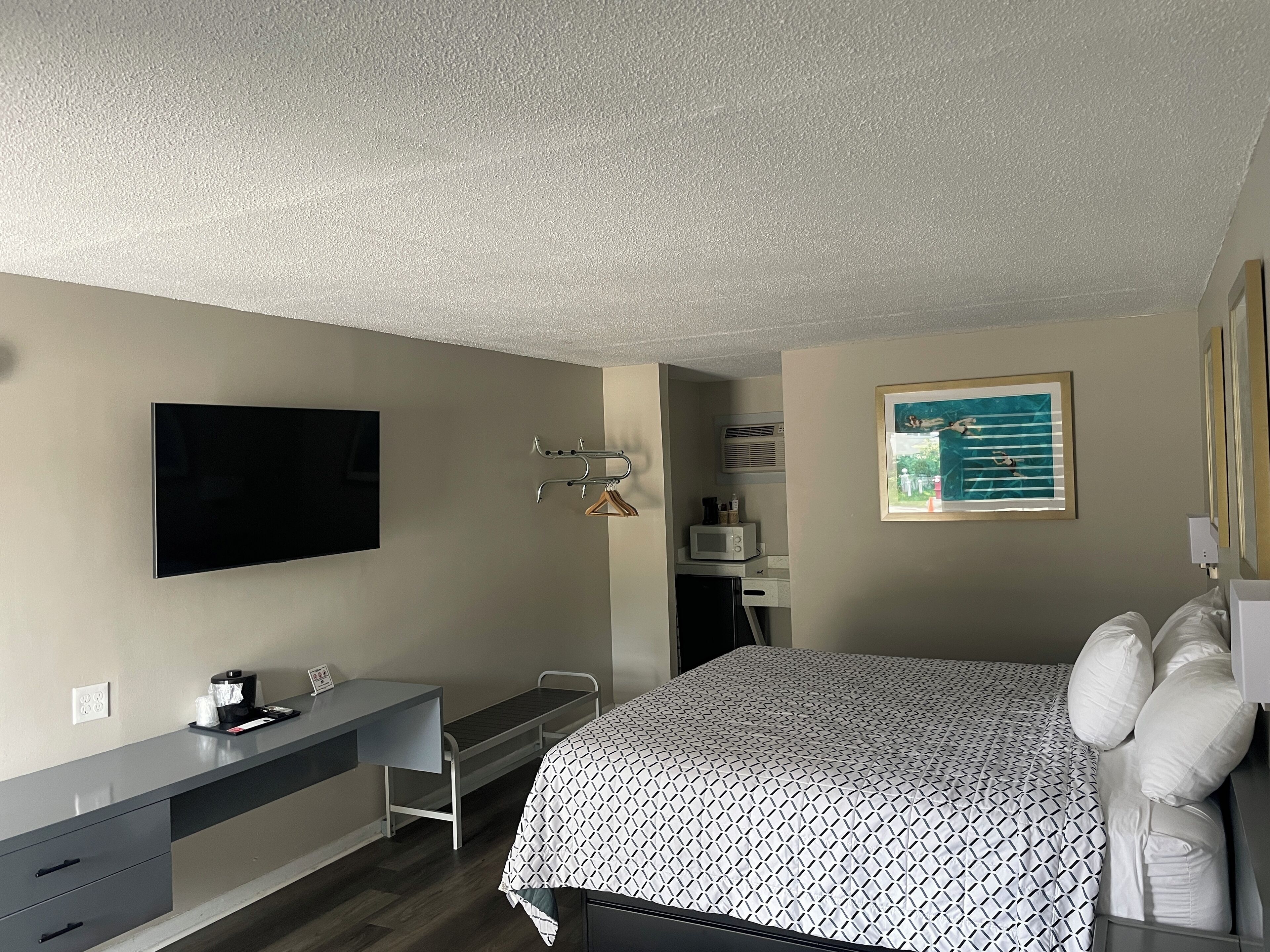 Une chambre d’hôtel équipée d’un lit, d’un bureau, d’une télévision, d’un tableau et d’un four à micro-ondes.