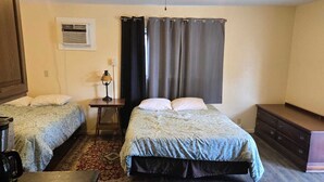 A bedroom with two beds, a desk, a dresser, and a rug. - Golden Door Motel (Traer)