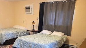 A bedroom with two beds, a rug, a lamp, and an air conditioning unit. - Golden Door Motel (Traer)