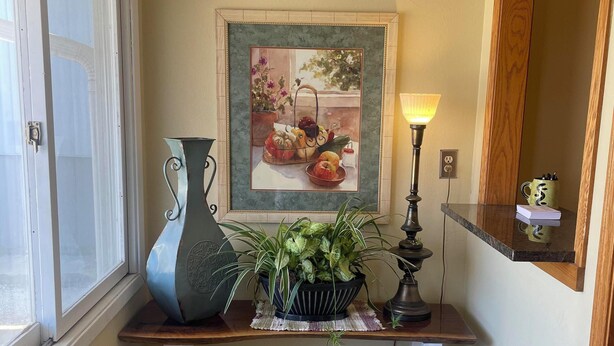 A hallway with a wooden bench, a framed painting, a potted plant, a lamp, and a mirror. - Golden Door Motel (Traer)