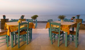 An outdoor seating area with tables and chairs, overlooking a body of water. - Socrates Seaside Apartments (Agios Nikolaos)
