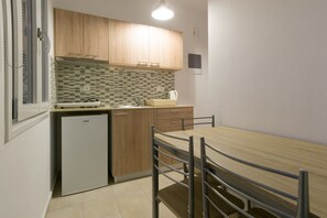 Cocina compacta con armarios de madera, un refrigerador pequeño, salpicadero de azulejos y una mesa de comedor con sillas.