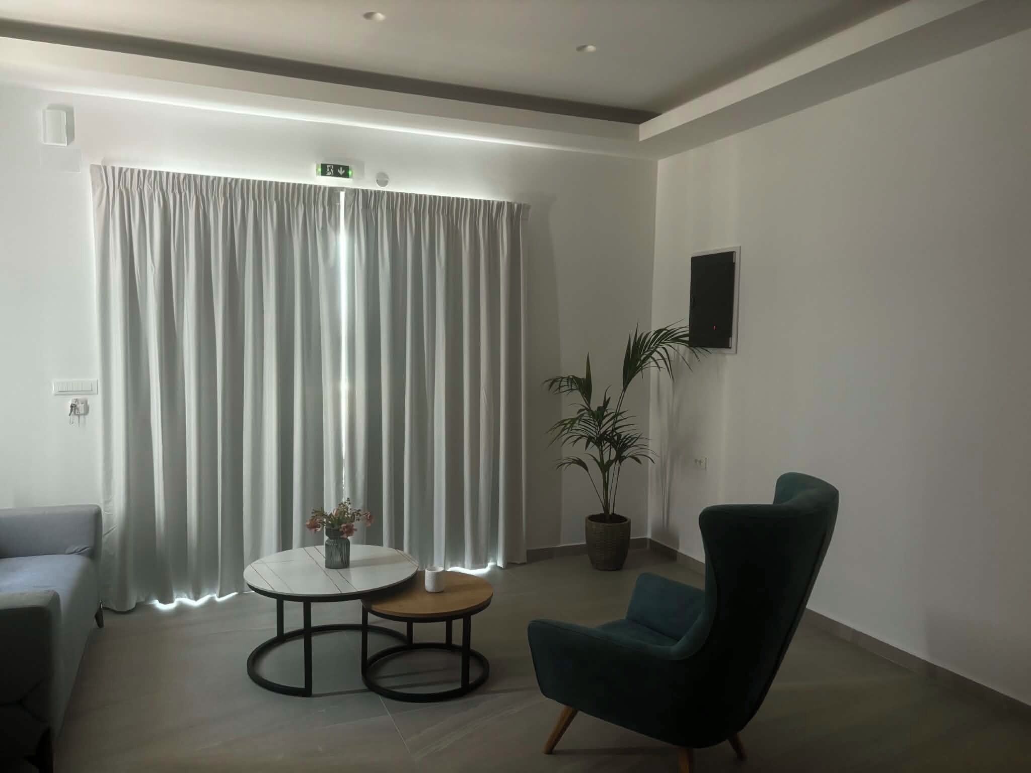 A modern room with a grey sofa, a round table with a vase, a potted plant, and a teal armchair.