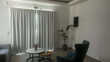 A modern room with a grey sofa, a round table with a vase, a potted plant, and a teal armchair.