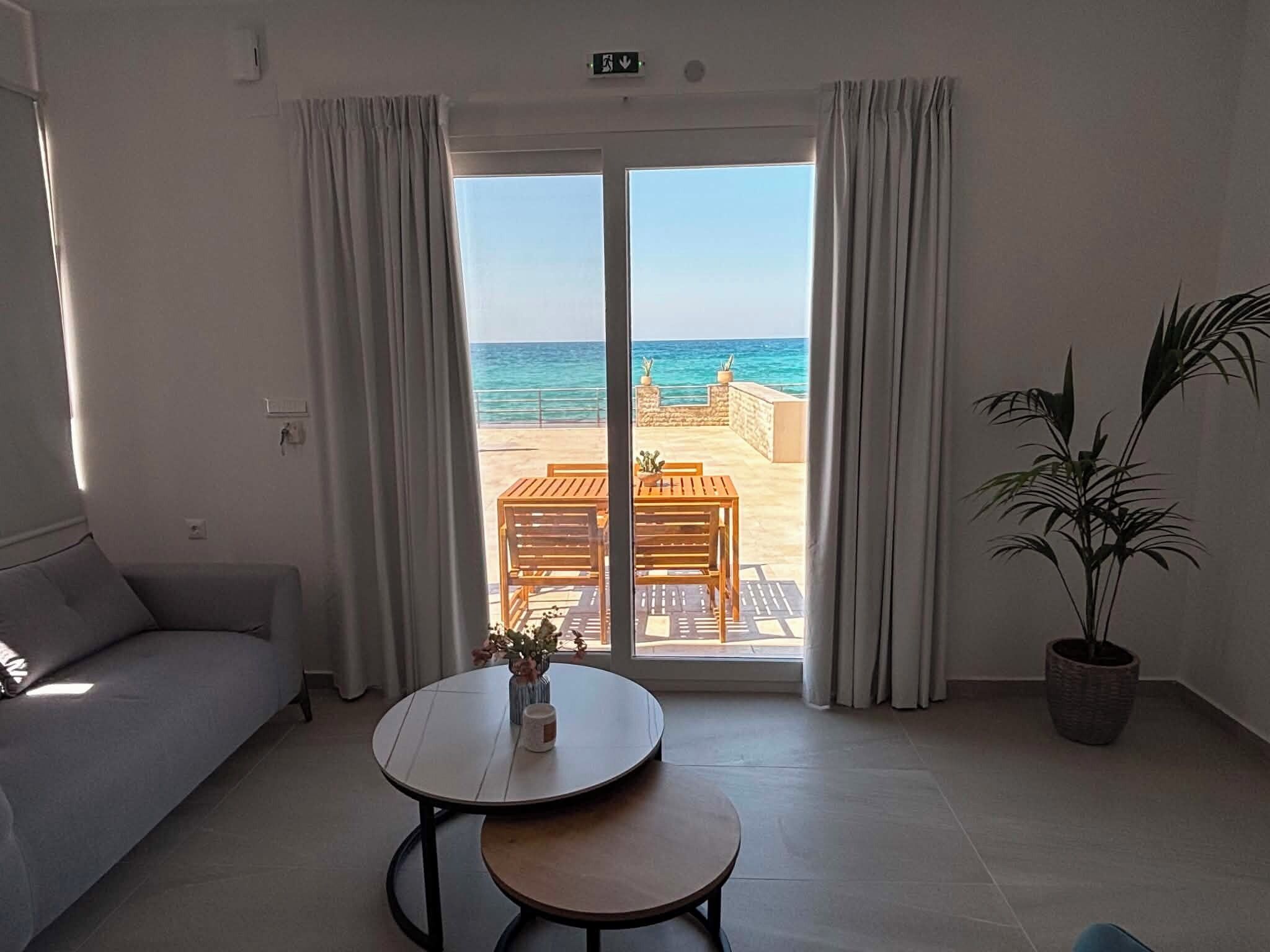 A room with a sofa, a round table with a vase, and a view of the beach through large sliding doors.