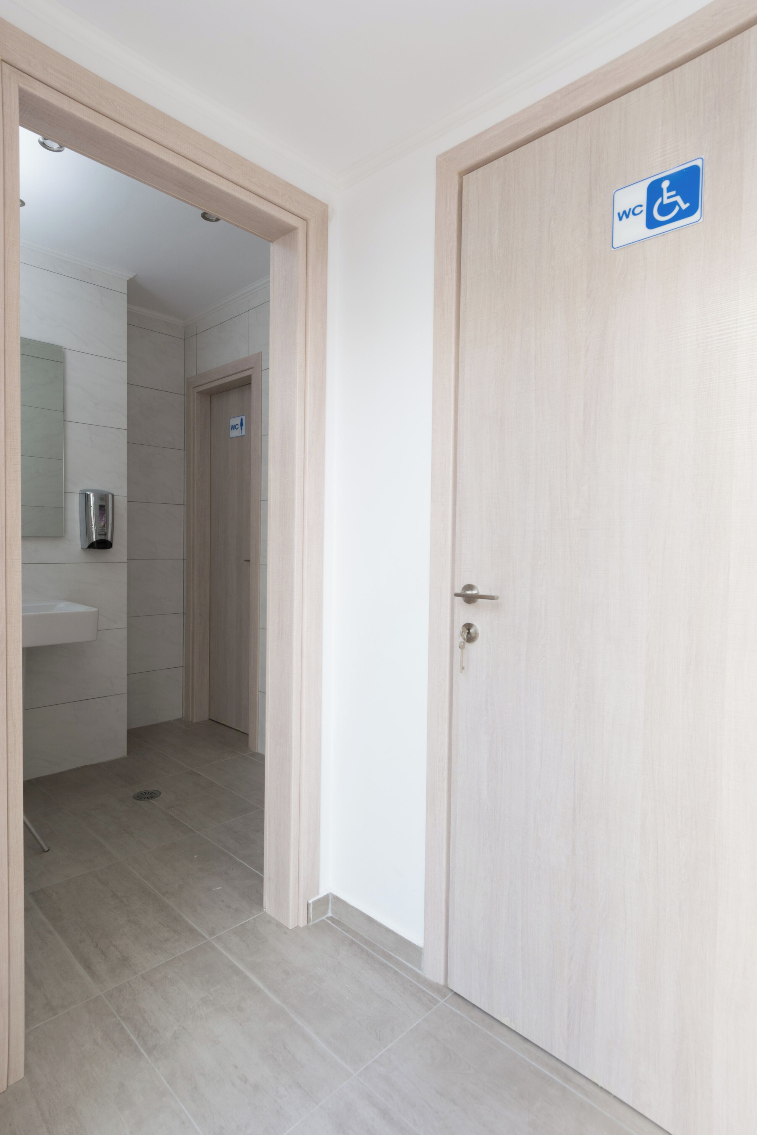 A hotel room with a wooden door, a WC sign, and a mirror.