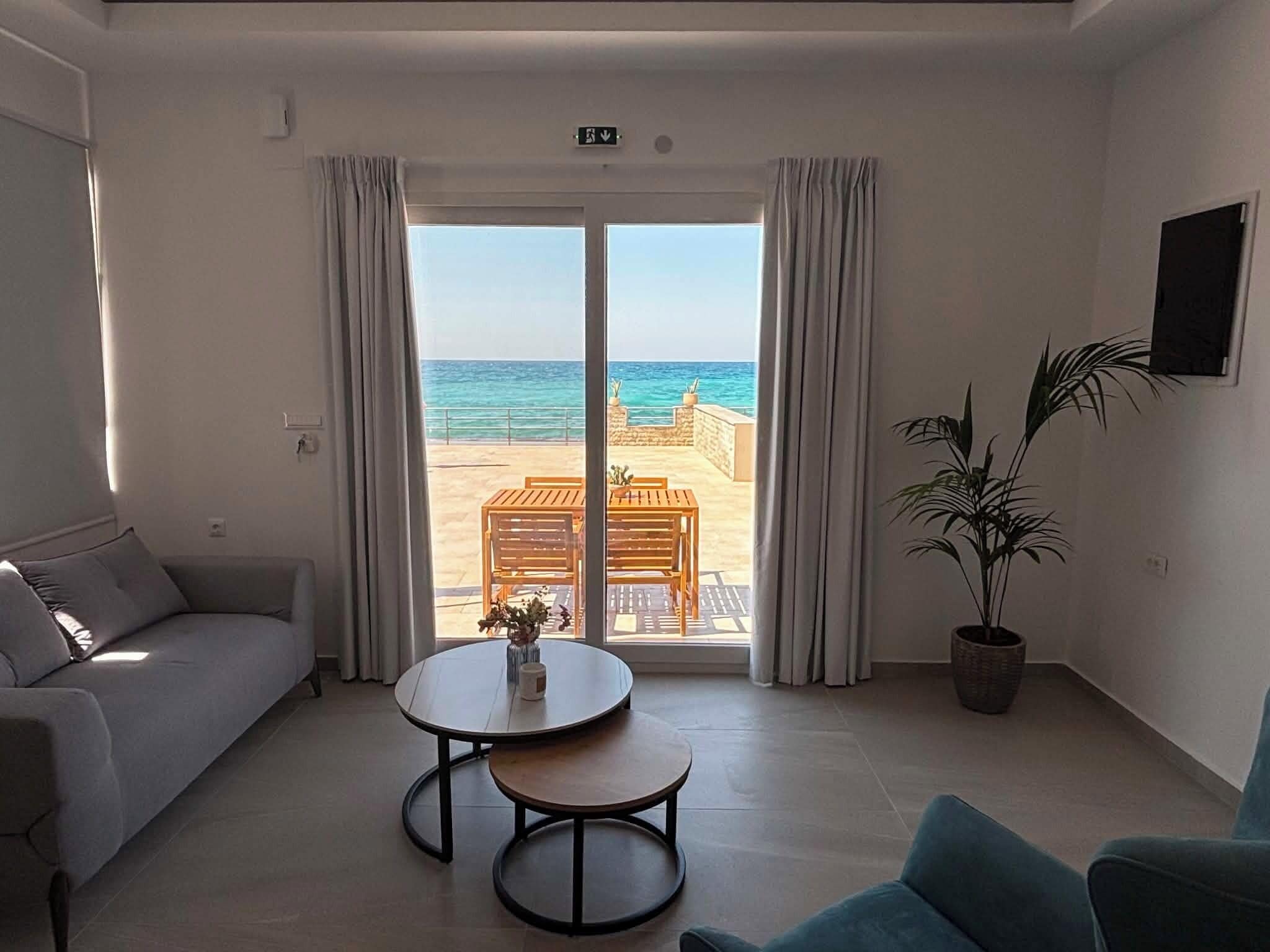 A room with a sofa, a small table, a potted plant, and a view of the beach through a sliding door.