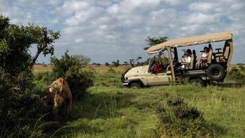 A safari vehicle with passengers observing wildlife in a grassy savannah.
