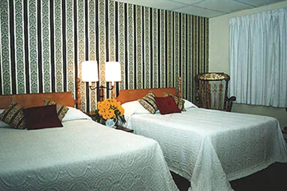 Ein Hotelzimmer mit zwei Betten, einem Nachttisch mit Lampe, einem Sessel und strukturierter Wandtapete.