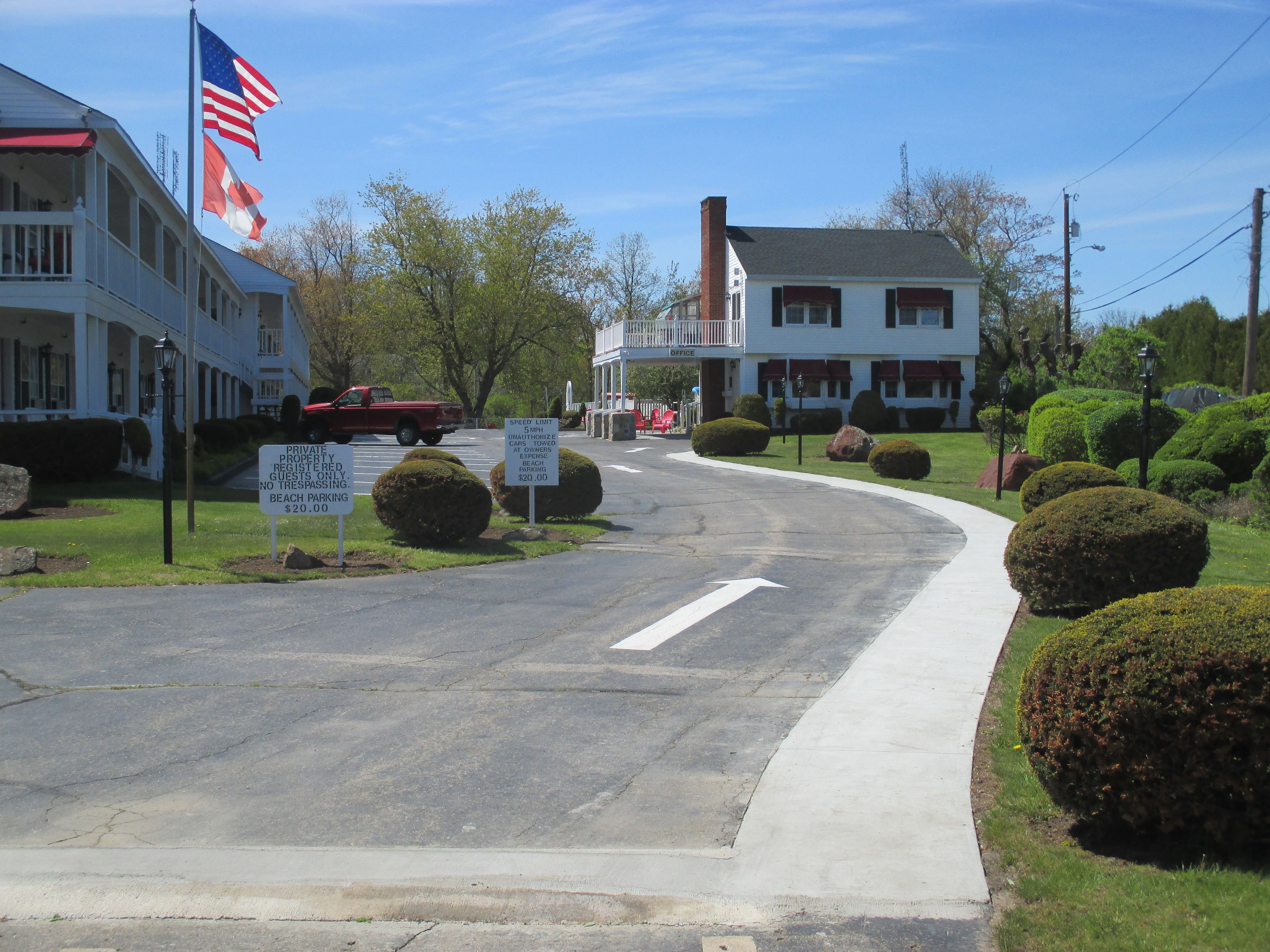 A street view with a building that has a flagpole with the American flag, a speed limit sign, and a sign indicating private property with beach parking.