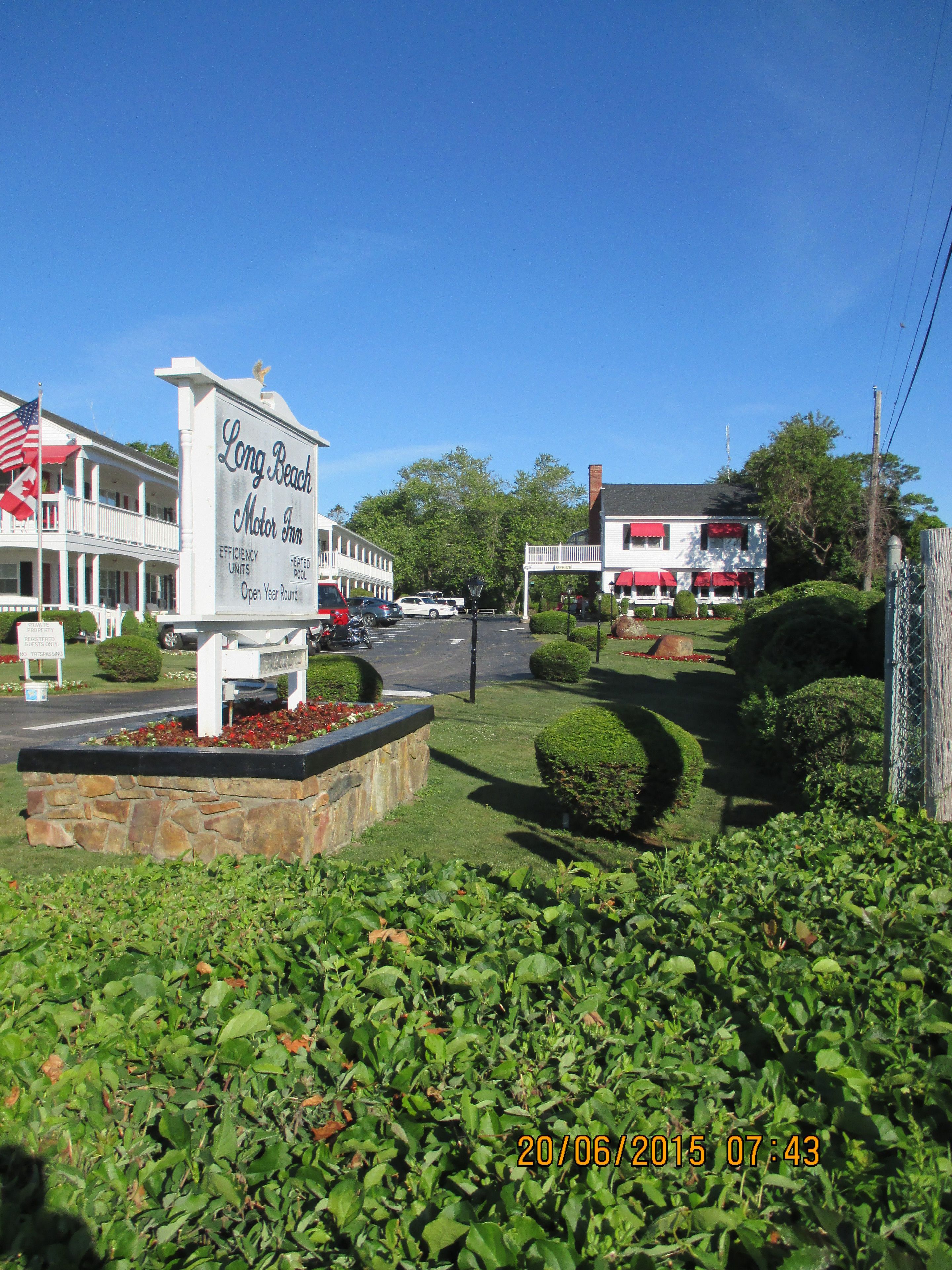A sign for Long Beach Motor Inn with a two-story building, a parking lot, and well-maintained landscaping.