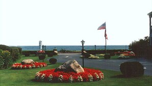 A landscaped garden with a pathway, a lighthouse, and an American flag. - Long Beach Motor Inn (York Beach)