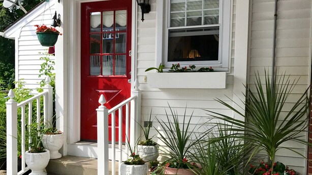 A white house with a red door, a window, and a porch with potted plants. - Long Beach Motor Inn (York Beach)