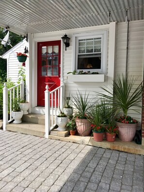 A white house with a red door, a window, and a porch with potted plants. - Long Beach Motor Inn (York Beach)