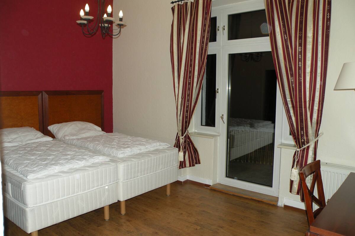 A bedroom with a double bed, a wooden headboard, a chandelier, and a window with curtains.