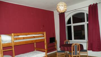A room with a bunk bed, a table with chairs, a window with curtains, and a hanging light fixture.