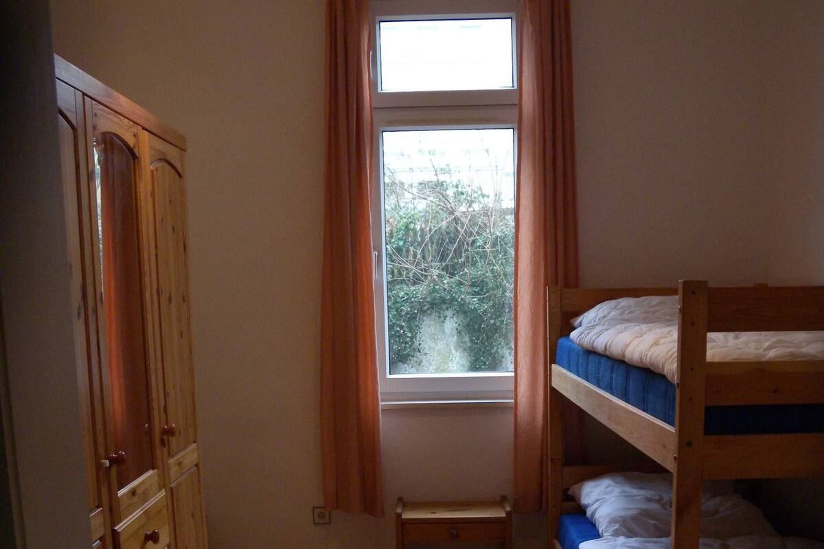 A room with a bunk bed, wooden wardrobe, and a window with curtains.