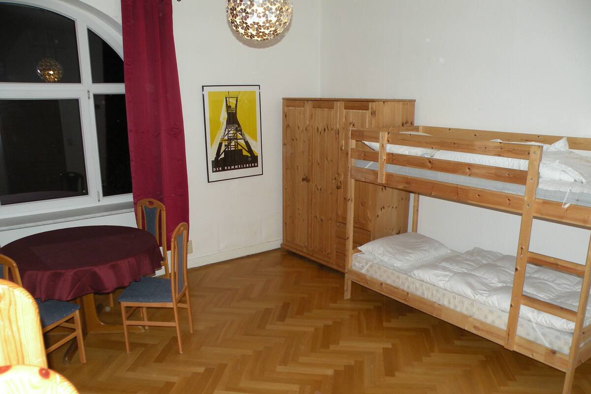 A room with a bunk bed, a wooden wardrobe, a desk with a chair, and a poster on the wall.