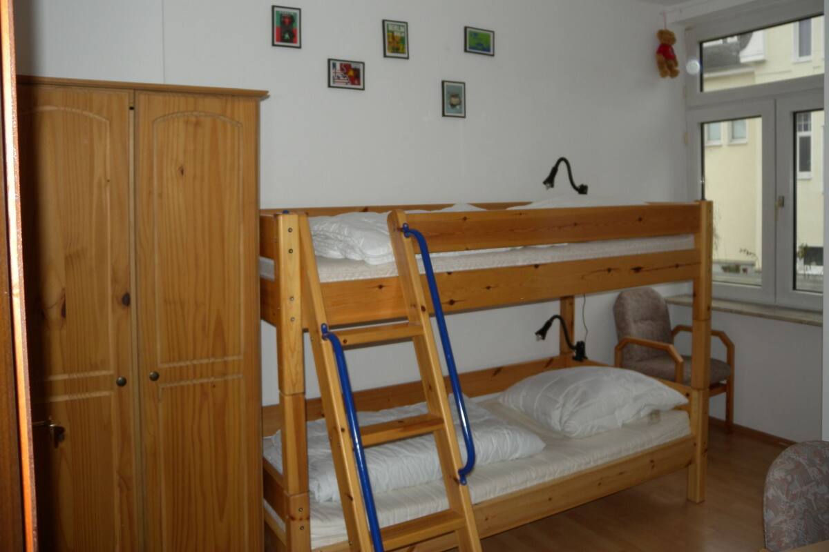 A bunk bed room with a wooden wardrobe, a window with a view, and several small pictures on the wall.