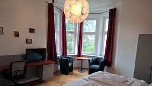 A hotel room with a bed, desk, chair, TV, and windows with curtains.