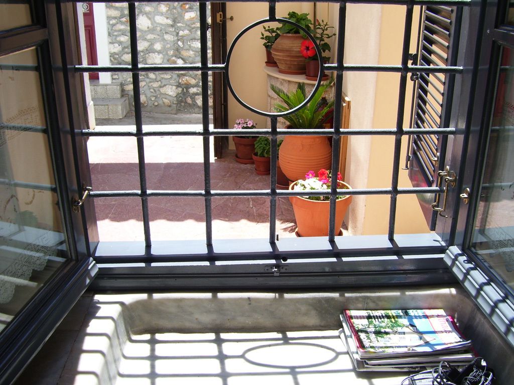 A view through a barred window with a tiled floor, a potted plant, and a book on the windowsill.