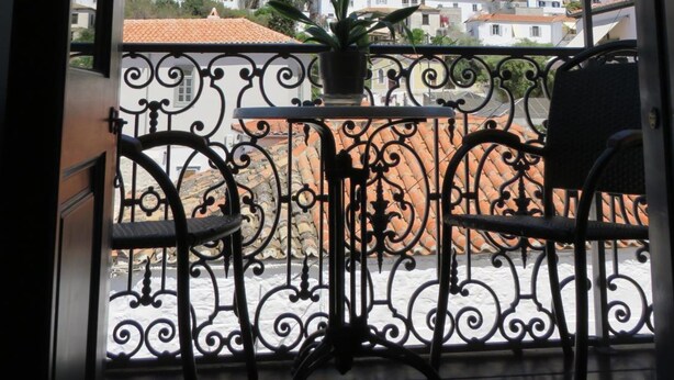 A balcony with a wrought iron railing, a potted plant, and a view of a hillside with buildings.