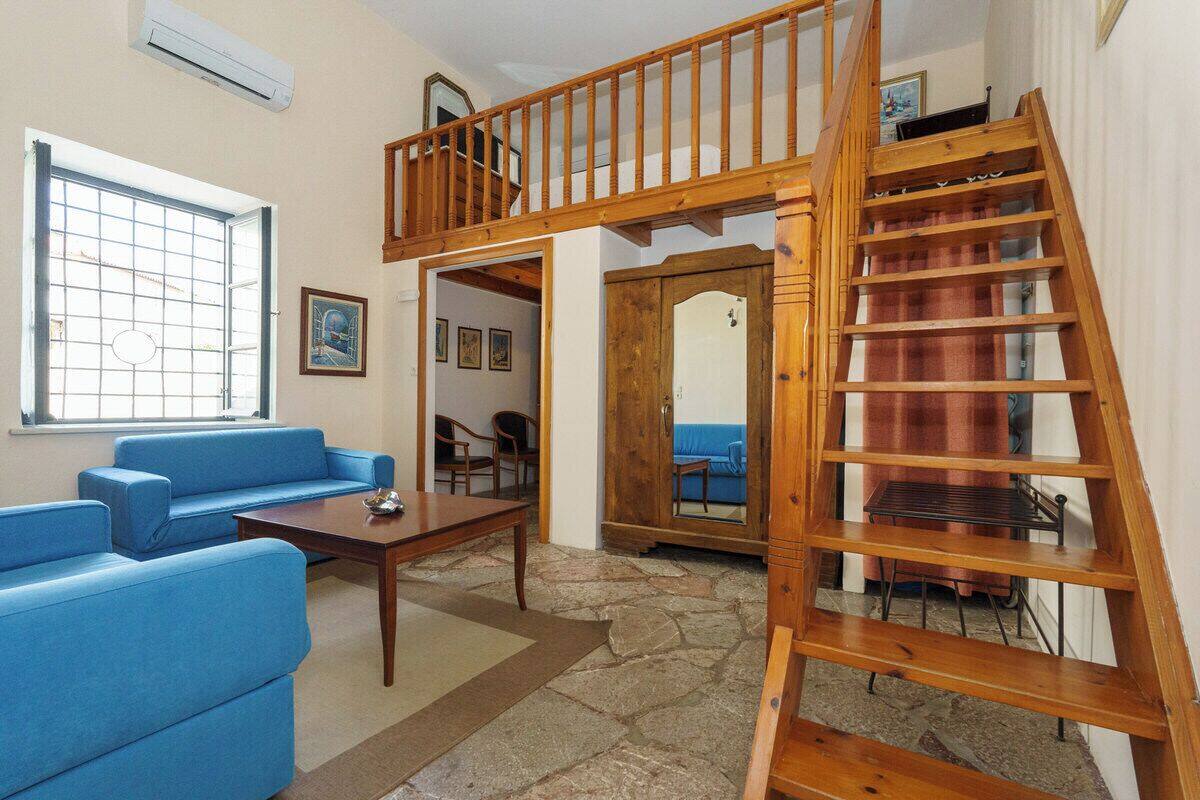 A room with a blue sofa, a wooden table, a staircase, and a view through a window.