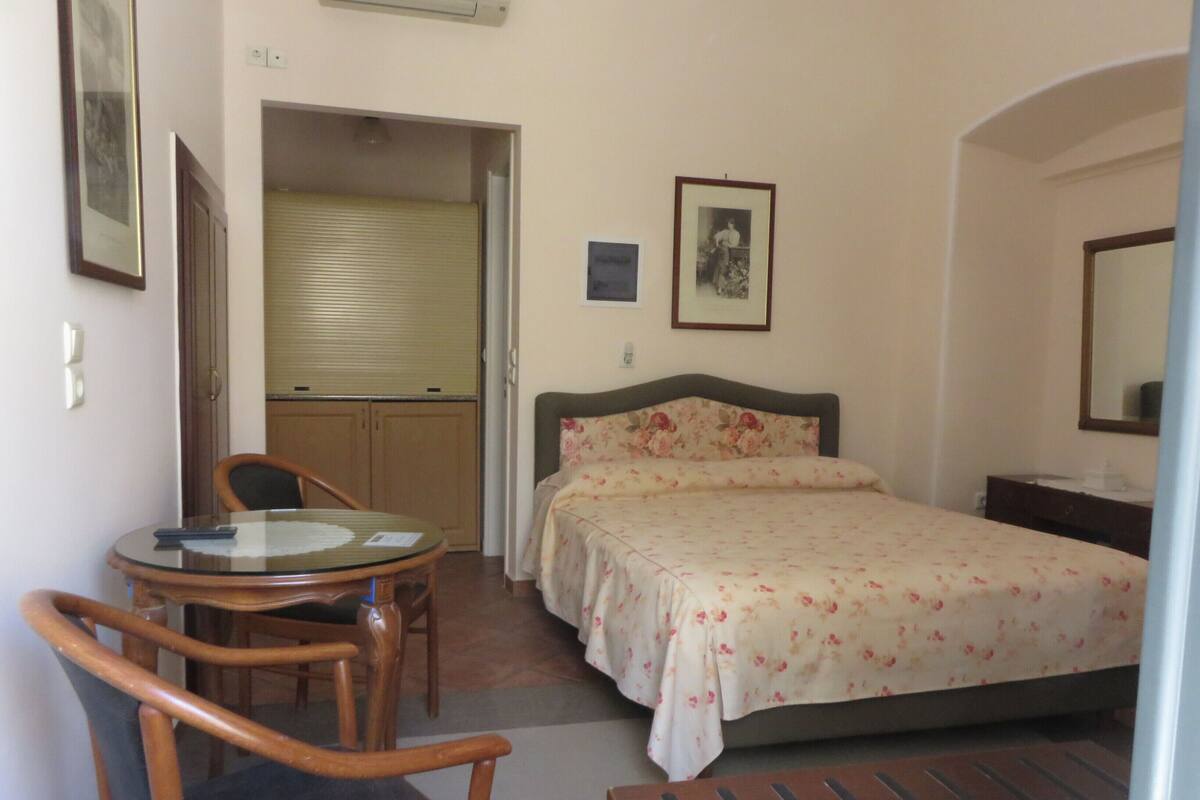 A hotel room with a bed, a small table with chairs, a desk, and a mirror.