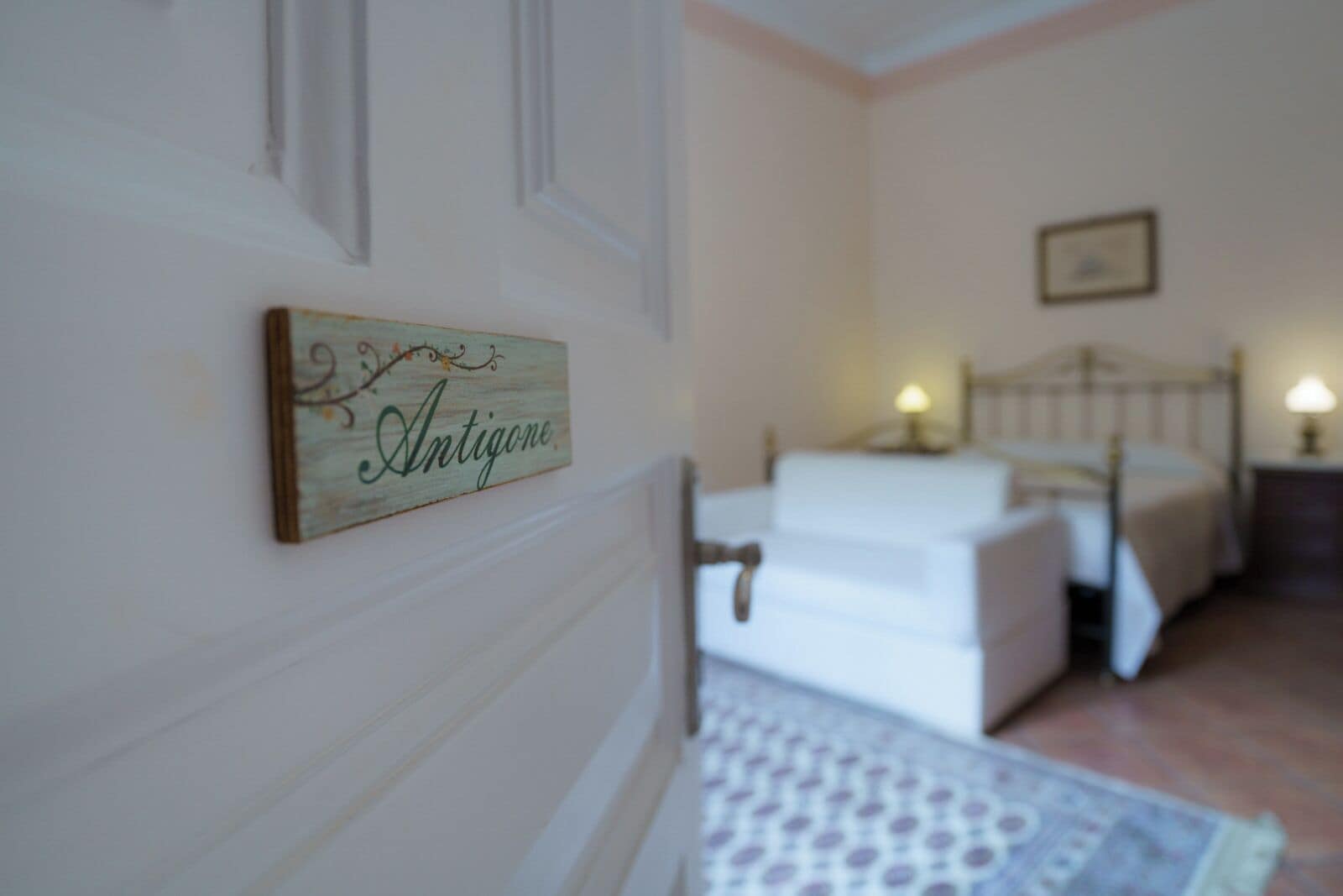Une chambre à coucher avec un lit, une table de chevet et un panneau fixé au mur sur lequel on peut lire « Antigone ».