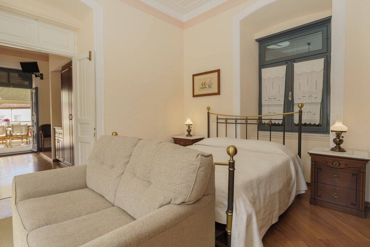 A bedroom with a bed, a nightstand, a dresser, a sofa, and a window with curtains.