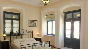 A bedroom with a bed, bedside tables, a bench, and two windows with shutters.