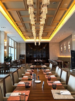 A spacious dining area with long tables, elegant chandeliers, and a modern interior design.