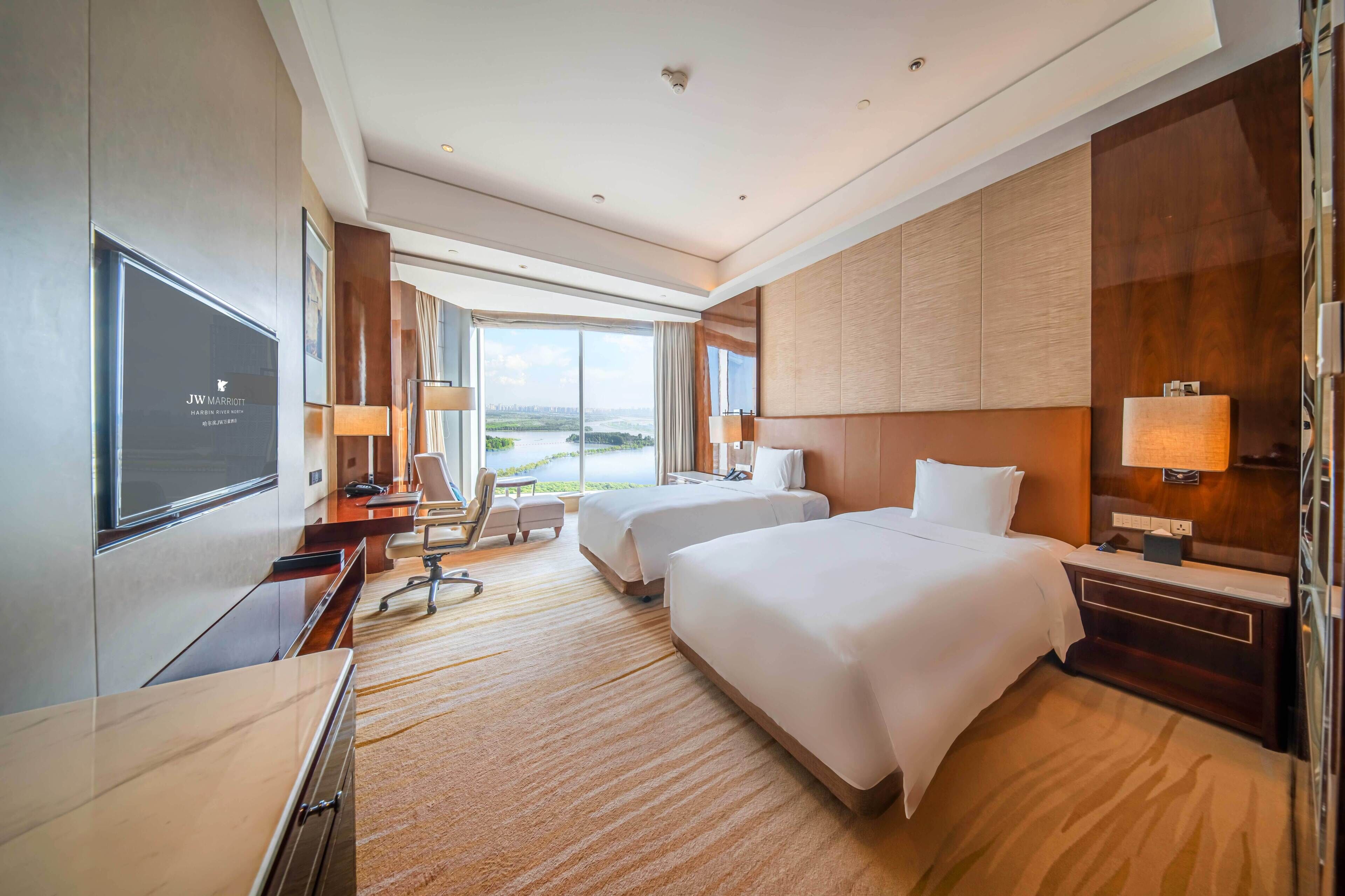 Habitación de hotel con una cama grande, un escritorio, una silla, un televisor y vistas a la ciudad.