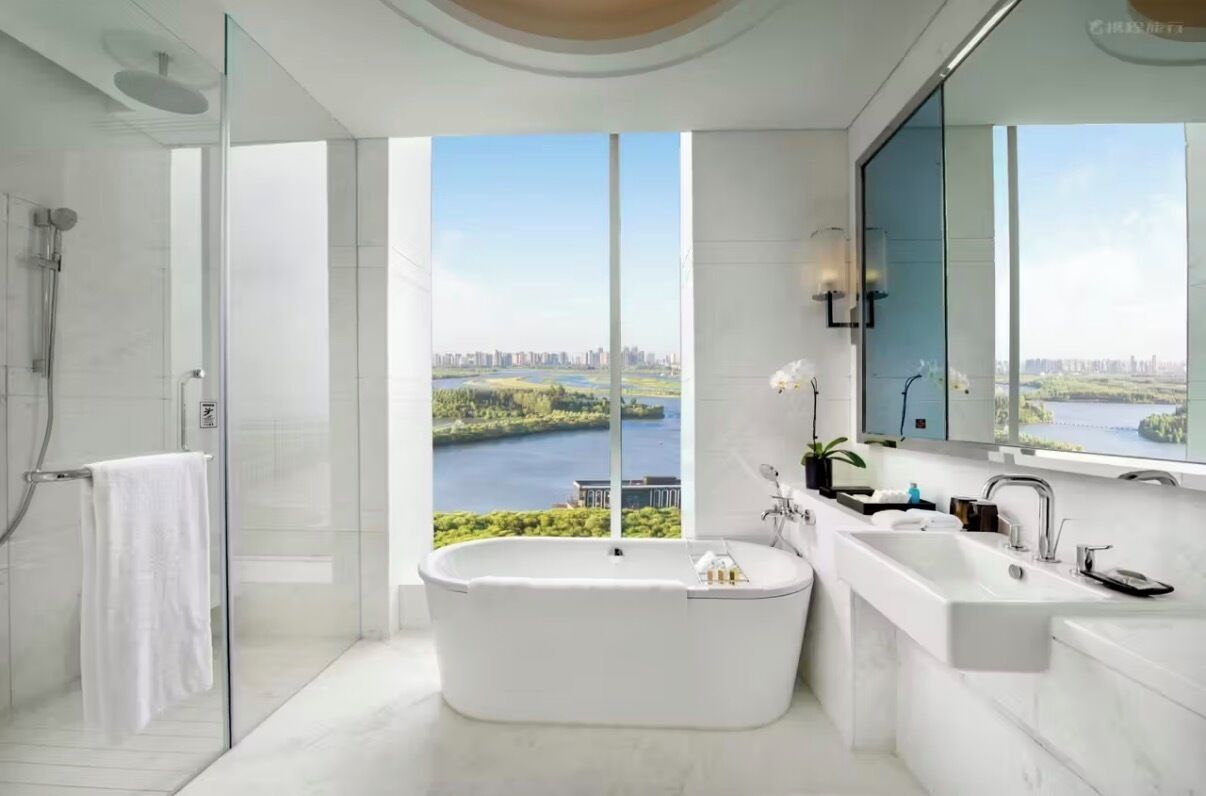 Un baño moderno con una bañera independiente, ducha con mampara de vidrio y un amplio ventanal con vistas a la ciudad.