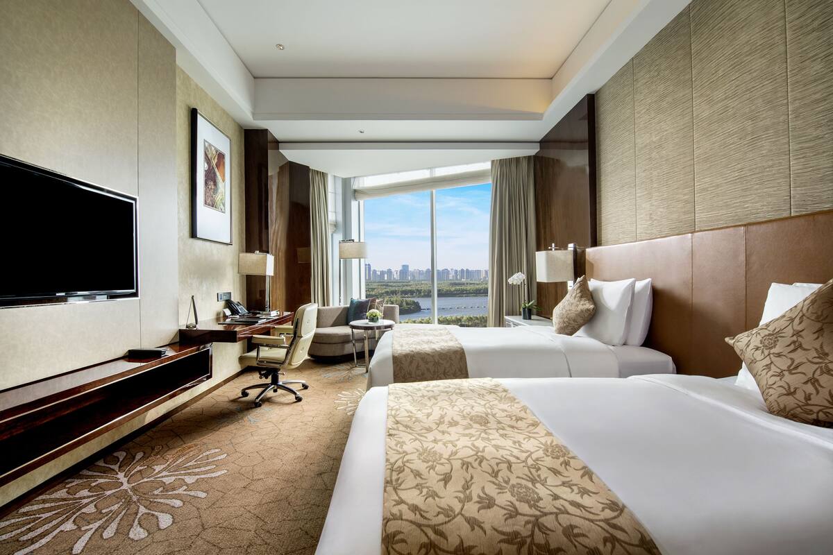 A hotel room with a large TV, two beds, a desk, and a view of the city.