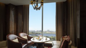 Una habitación con vista a un puente y al agua, una mesa redonda con un florero, dos sillones de cuero y un sofá con cojines.