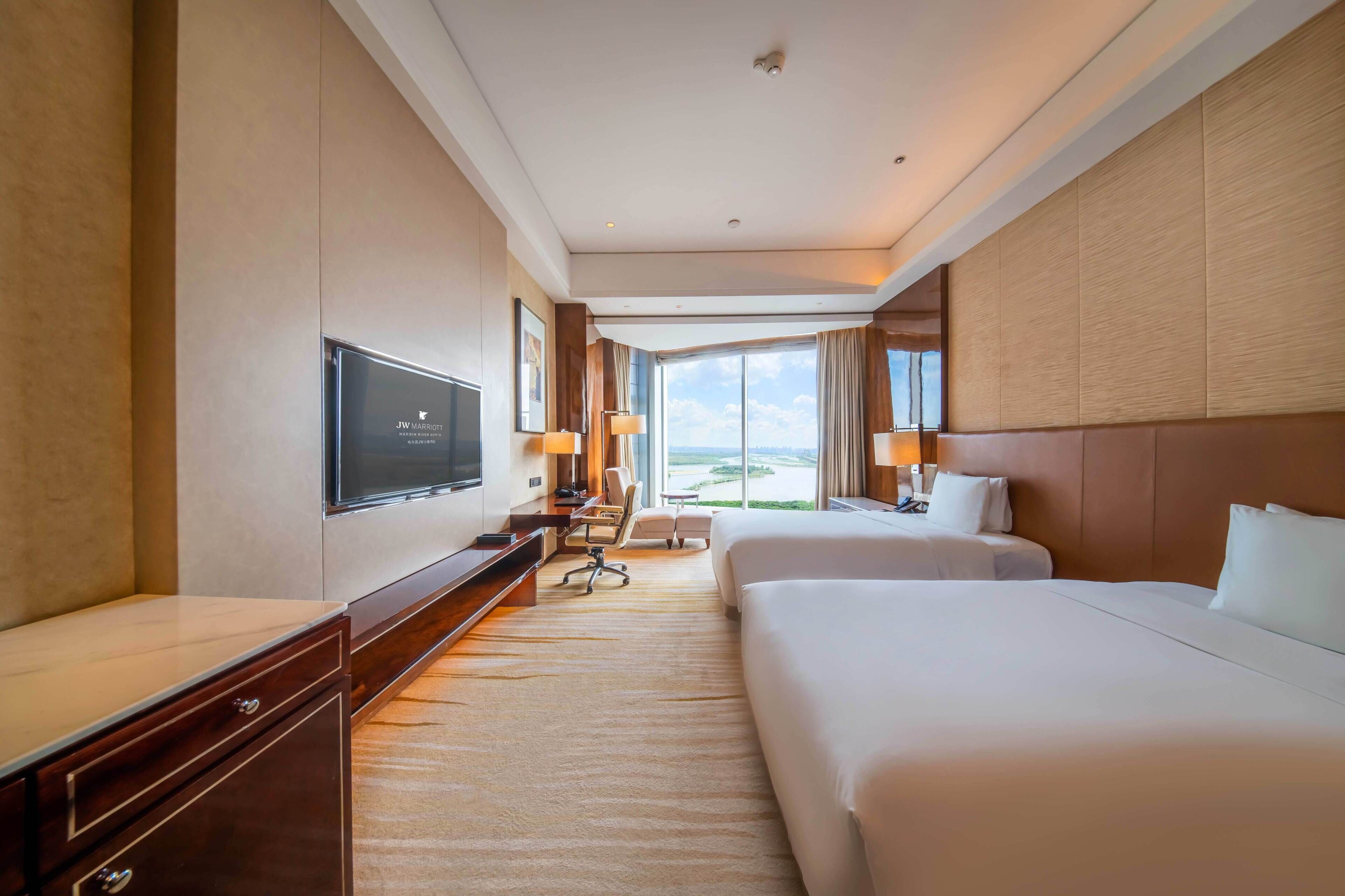 A hotel room with a large bed, a smaller bed, a desk, a TV, and a view of the outdoors.