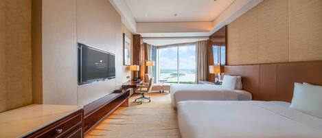 A hotel room with a large bed, a smaller bed, a desk, a TV, and a view of the outdoors.