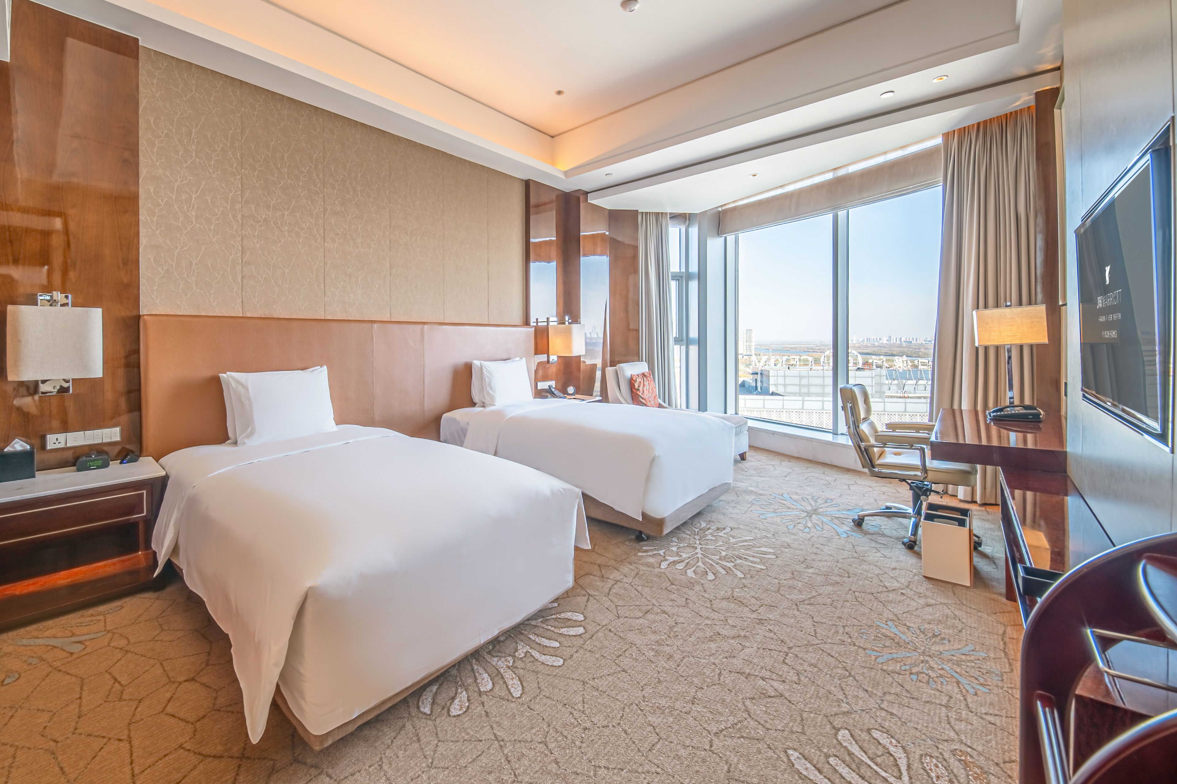 Habitación de hotel con dos camas, un escritorio, una silla, un televisor y un ventanal con vistas a la ciudad.
